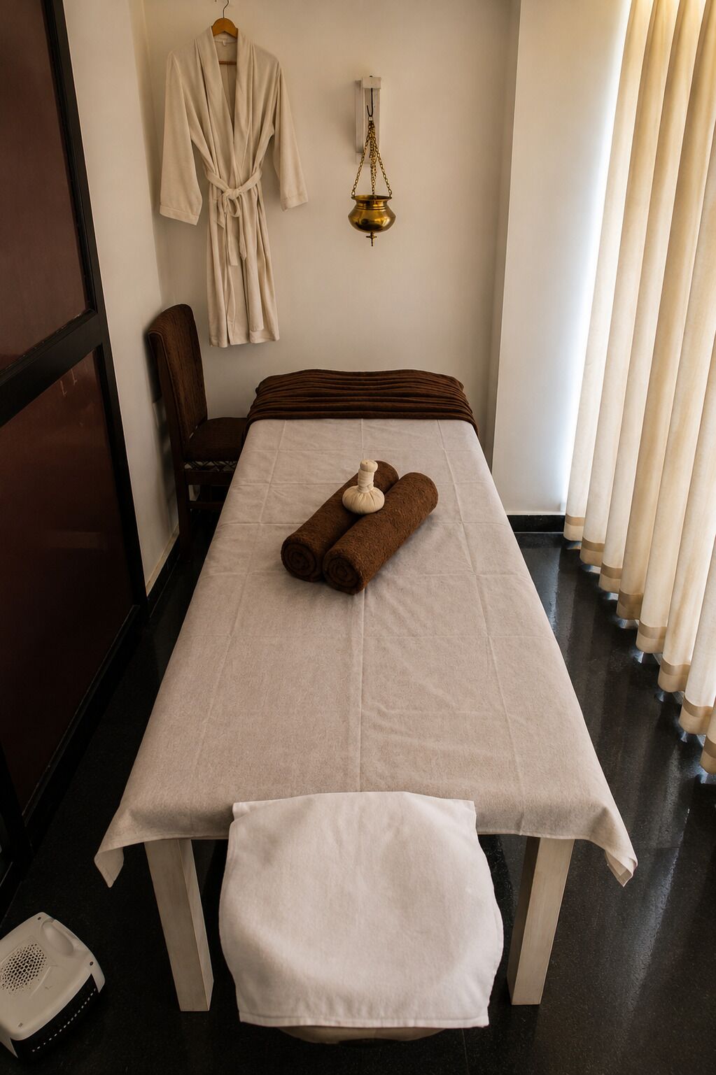A room with a bed, a bench, a hanging robe, and a wall-mounted lamp.