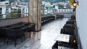 An outdoor seating area with tables and chairs, a decorative light structure, and a view of a cityscape in the background. - Royalistiq (Rishikesh)