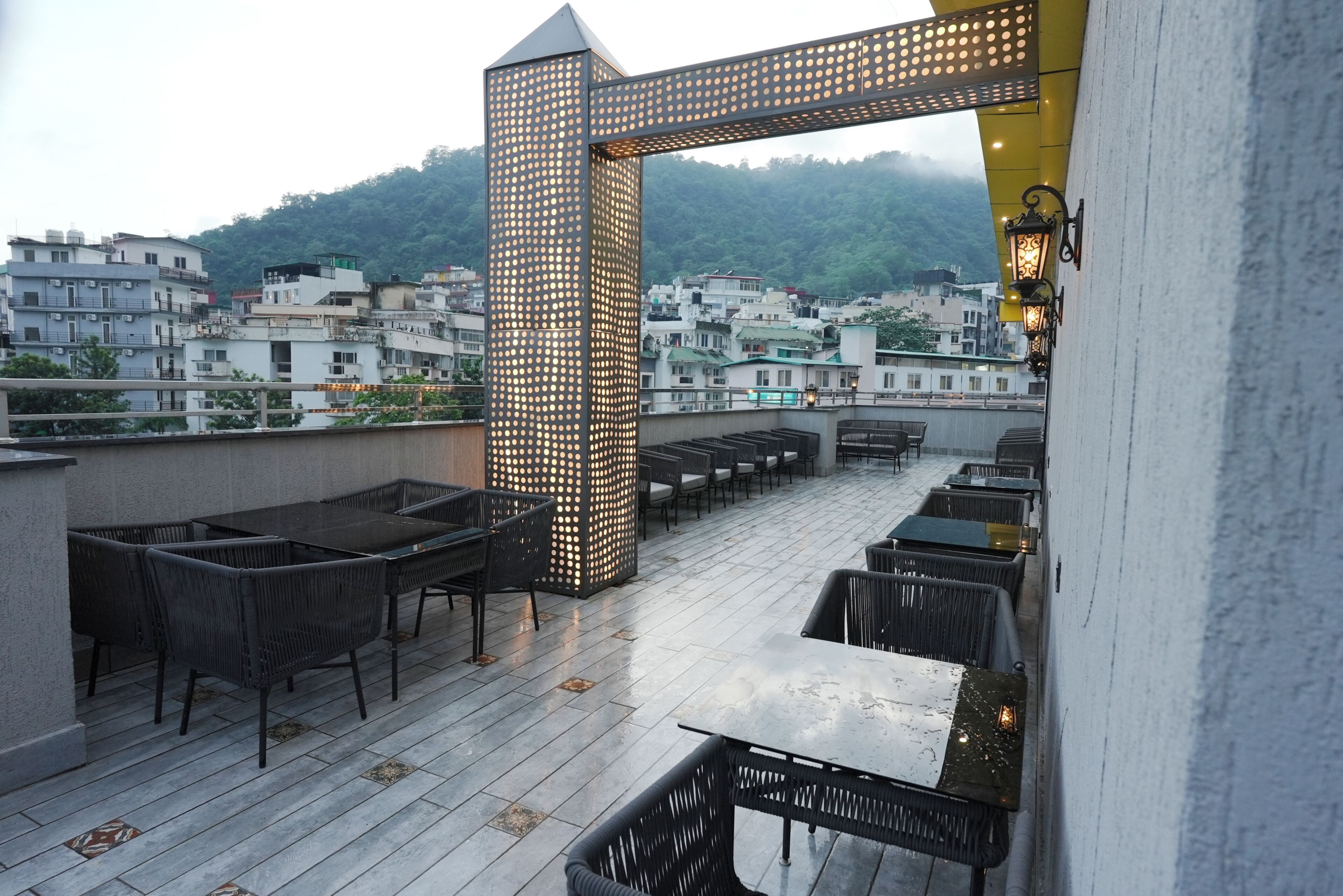 Un espacio al aire libre con mesas y sillas, un arco de metal decorativo y vistas a una zona residencial de fondo.