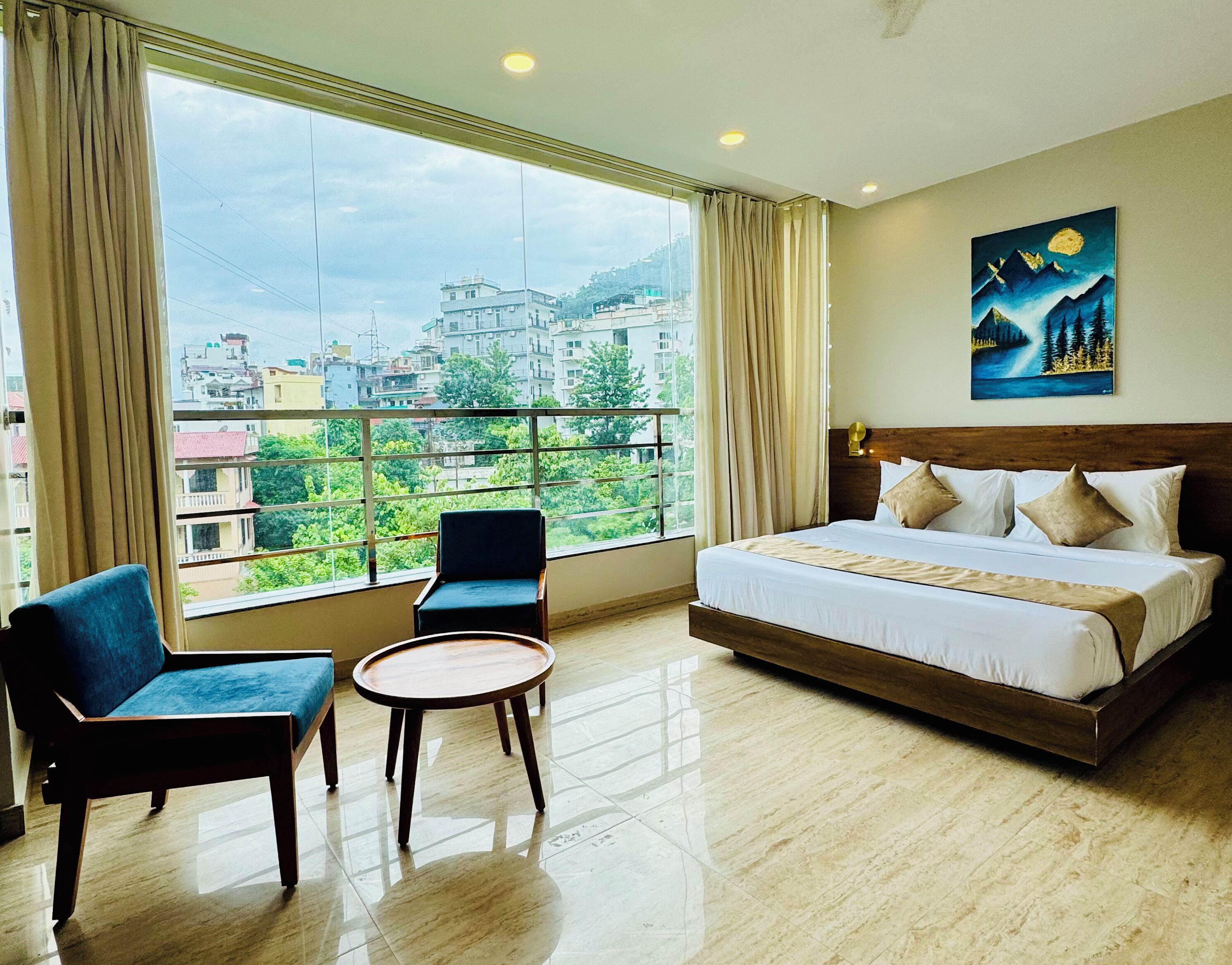 A hotel room with a large window, a bed, two chairs, and a small table.
