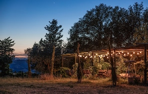 Ein Sitzbereich im Freien mit Lichterketten, umgeben von Bäumen und Blick auf die Landschaft.