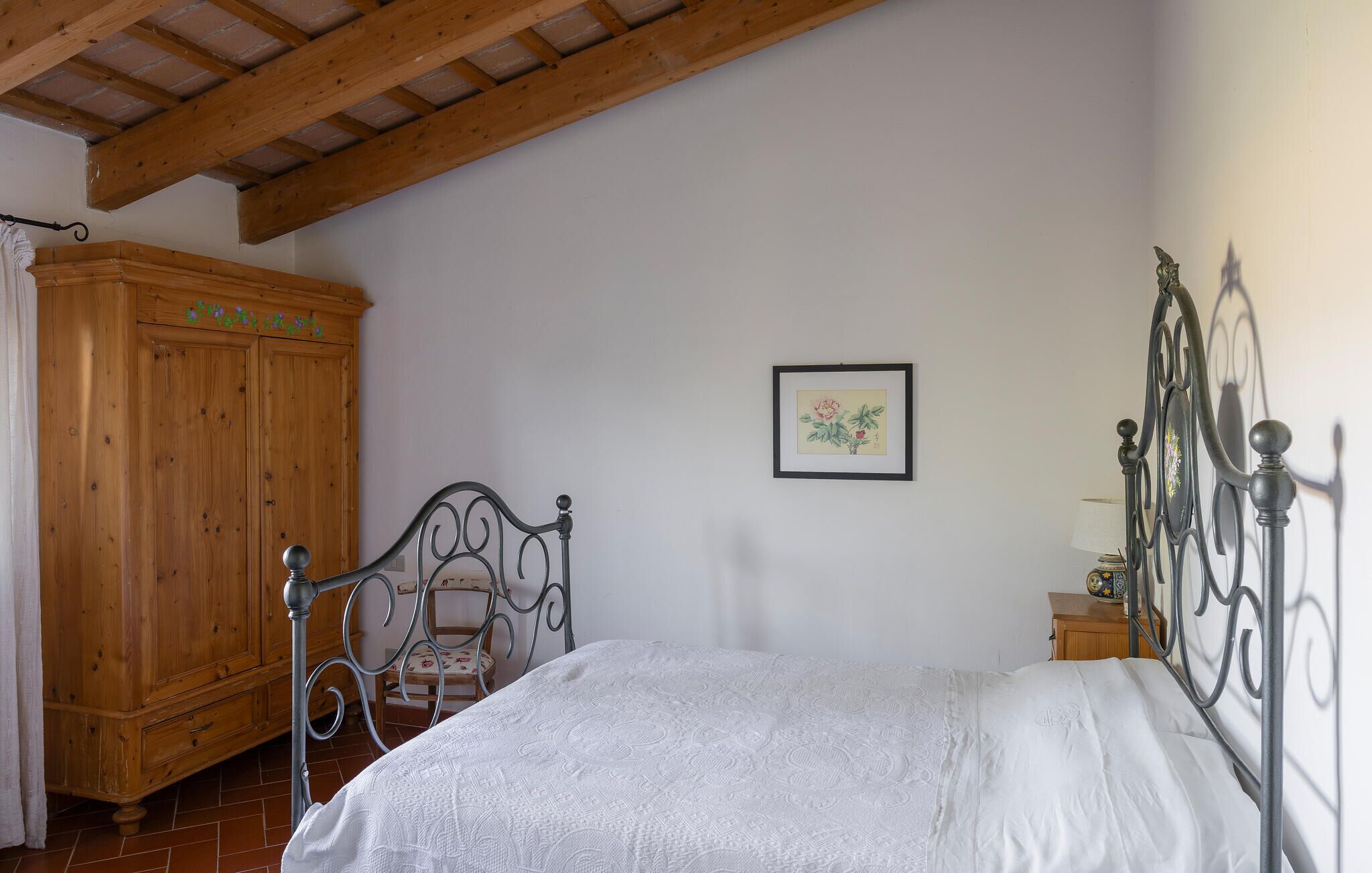 A bedroom with a bed, a wooden wardrobe, a chair, and a framed picture on the wall.