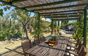 An outdoor patio with a wooden table and chairs, surrounded by potted plants and a pergola structure. - Lovely home in Cinigiano (Cinigiano)