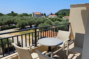 Ein Balkon mit Korbmöbeln und einem Tisch, mit Blick auf einen Parkplatz und Grünflächen.