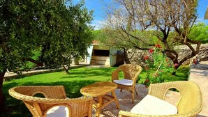An outdoor seating area with wicker furniture and a stone table, surrounded by greenery and a stone wall. - Coastal Breeze House - House (Selca)
