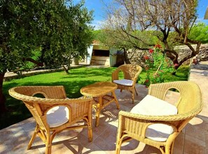 An outdoor seating area with wicker furniture and a stone table, surrounded by greenery and a stone wall. - Coastal Breeze House - House (Selca)