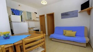 A compact living space with a kitchenette, a dining table with chairs, a sofa, and a television on a stand. - Coastal Breeze House - House (Selca)