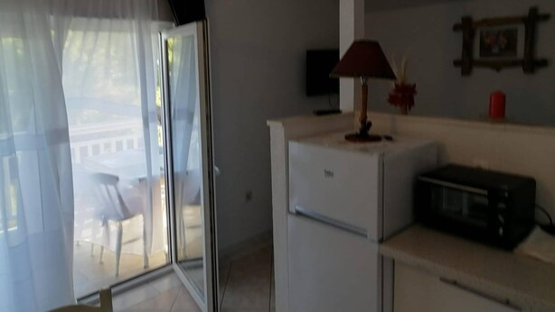 Ein Zimmer mit einer Schiebeglasdoor, einem an der Wand montierten Flachbildfernseher, einer Mikrowelle auf der Arbeitsplatte und einem kleinen Tisch mit einem Stuhl.