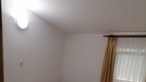 Ein Einzelbett mit hölzernem Kopfteil, ein Nachttisch, eine Heizung und ein Fenster mit Vorhängen.