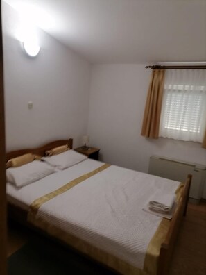 A single bed with a wooden headboard, a nightstand, a radiator, and a window with curtains. - Apartments Libertas - Two Bedroom Apartment With Balcony and Sea View - (Rogoznica)