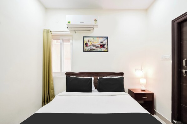 A hotel room with a bed, a nightstand, a lamp, a painting, and an air conditioning unit. - Super Collection O Madhapur (Hyderabad)
