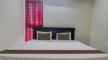 A single bed with a headboard, two pillows, and a white bedspread with a red trim.