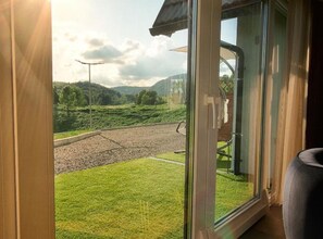 Ein Zimmer mit großem Fenster und Blick auf eine Wiese sowie eine Straße.