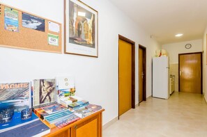 A corridor with a corkboard displaying travel information, a framed artwork, and a desk with various travel magazines. - Apartments Botica- Double Room (Zupa dubrovacka)