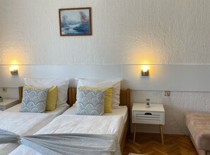 A bedroom with two beds, a bedside table with a lamp, a nightstand, and a painting on the wall. - Standard Twin 2 (Rakovica)