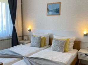 A double bed with two pillows, a bedside table, a wall-mounted picture, and a window with curtains. - Standard Twin 2 (Rakovica)