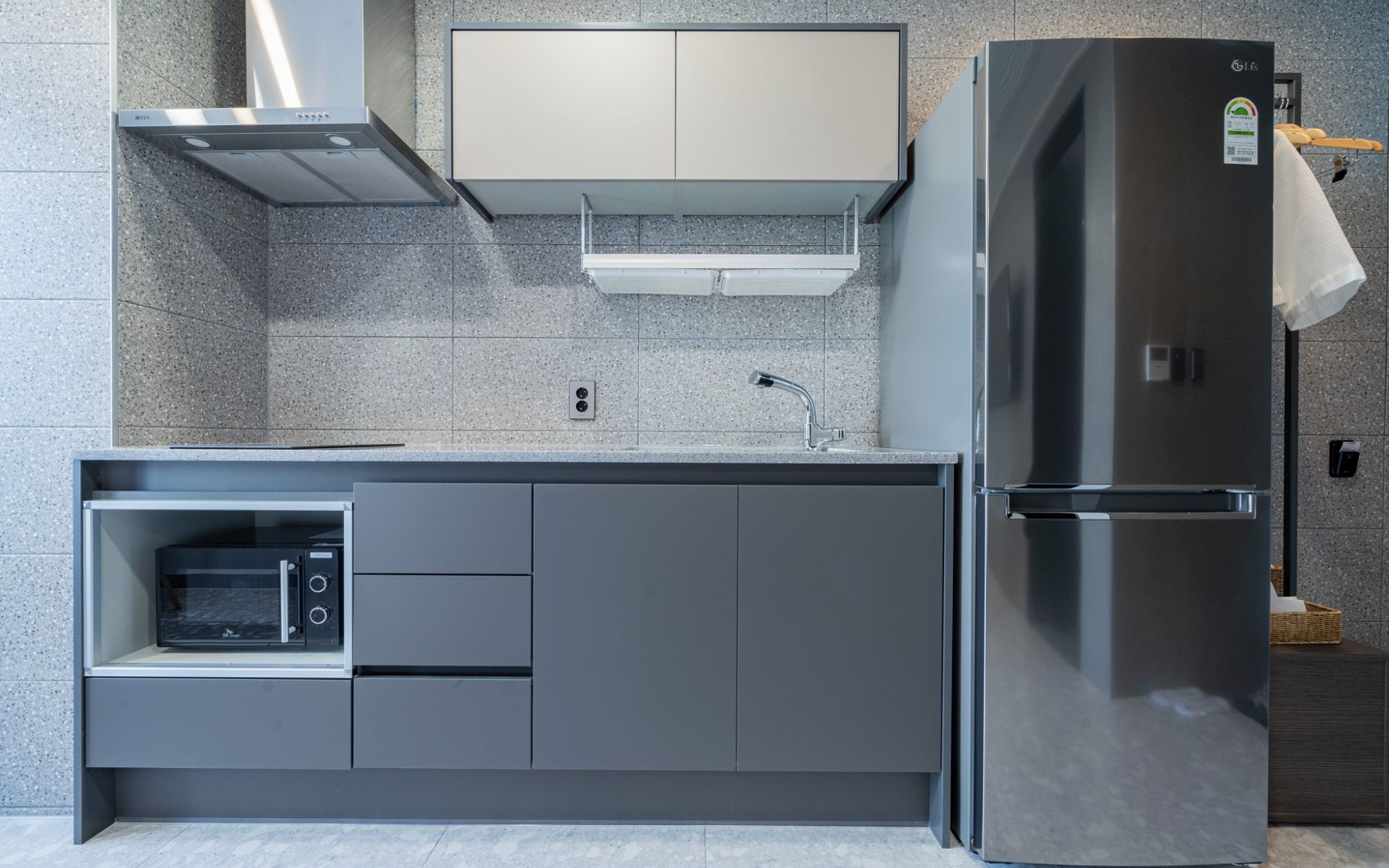 A modern kitchen with a built-in microwave, a stainless steel refrigerator, and a grey cabinet.