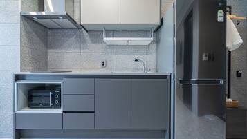 A modern kitchen with a built-in microwave, a stainless steel refrigerator, and a grey cabinet.