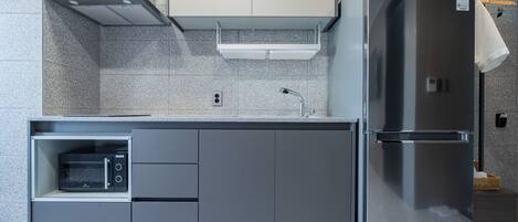 Una cocina moderna con microondas integrado, refrigerador de acero inoxidable y un armario gris.