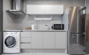 A modern kitchen with a stainless steel refrigerator, a microwave, a washing machine, and a built-in oven.