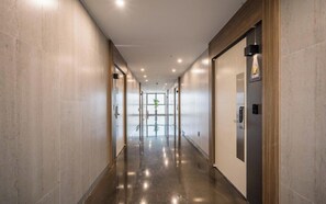 Un pasillo moderno de hotel con piso pulido, puertas de vidrio y un ascensor visible a la derecha.