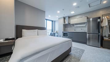 Habitació d'hotel moderna amb un llit gran, un escriptori amb telèfon, una cuineta amb nevera i una finestra amb vistes.