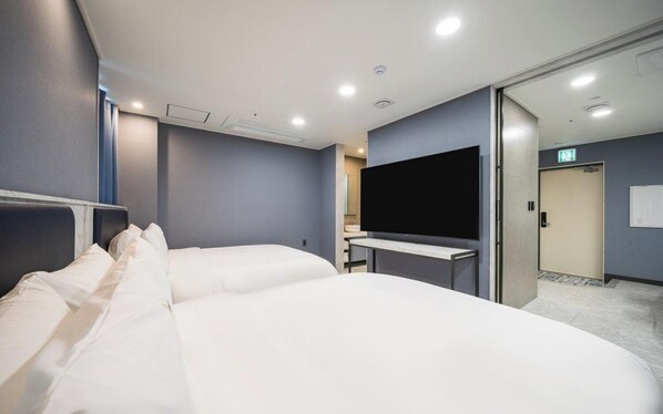 A hotel room with two beds, a flat-screen TV, a desk, and a bathroom visible through an open door.