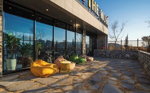 Un edificio con un amplio ventanal de vidrio, mobiliario exterior con cojines y un patio empedrado de piedra.