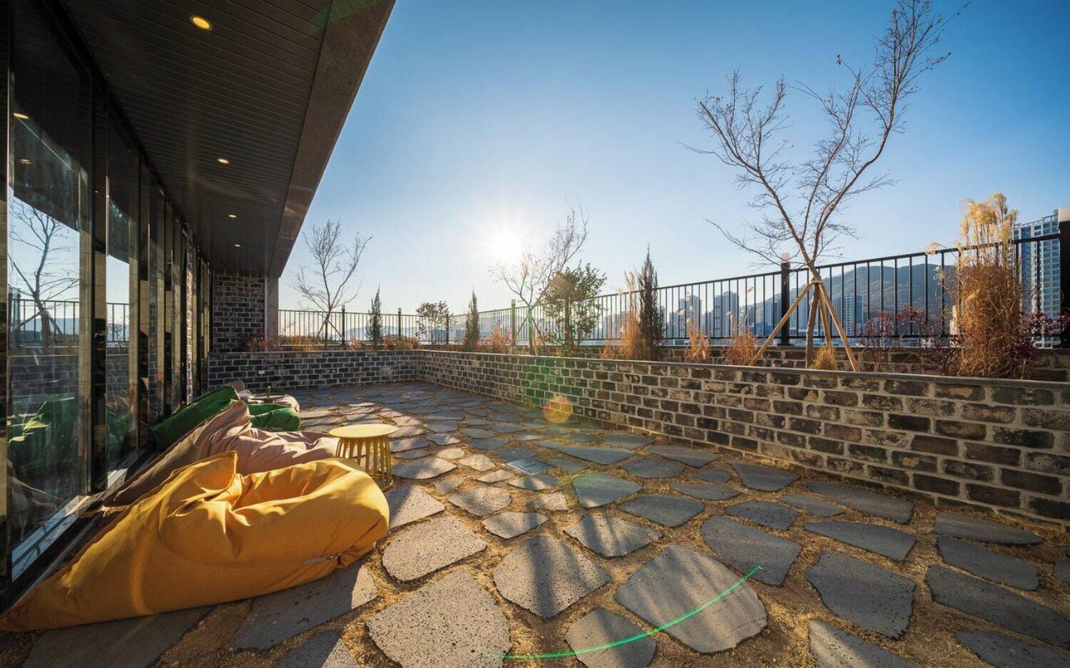 Un patio exterior con piso de piedra, un sillón de mezcla relajado amarillo y una pequeña mesa redonda.
