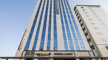 A tall hotel building with a modern design, featuring a prominent sign for The Muse Hotel and a visible parking area.