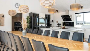 A modern kitchen with a central island, black appliances, and a dining area with a long wooden table and chairs. - Pet friendly home in Harboøre with sauna (Harboøre)