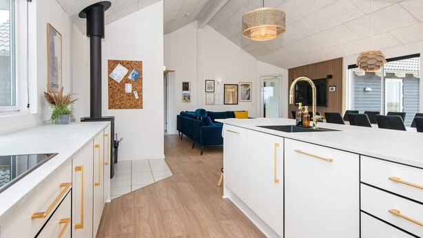 A modern kitchen with white cabinetry, a central island, and a dining area with a blue sofa. - Pet friendly home in Harboøre with sauna (Harboøre)