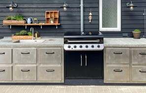 Eine Außenküche mit integriertem Grill, Stauraumschränken und einem Fenster mit Blick.
