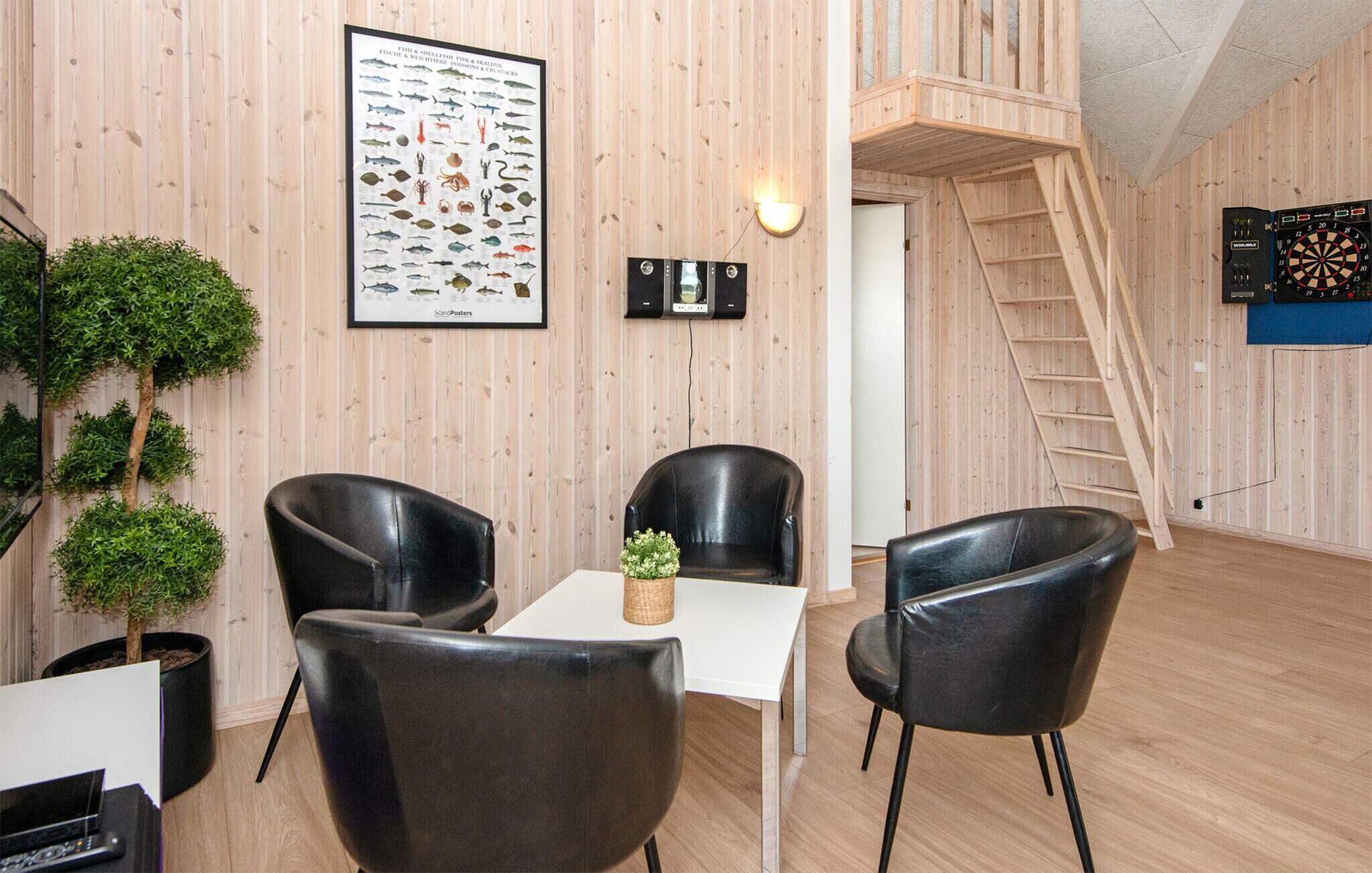 Ein Zimmer mit Holzwandverkleidung, einem gerahmten Poster mit einem Fischmotiv, einem kleinen Tisch mit einer Topfpflanze und einer Leiter, die zu einer erhöhten Ebene führt.