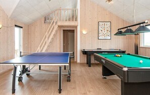 Ein Raum mit Tischtennisplatte, Billardtisch und einer Treppe zu einer oberen Ebene.