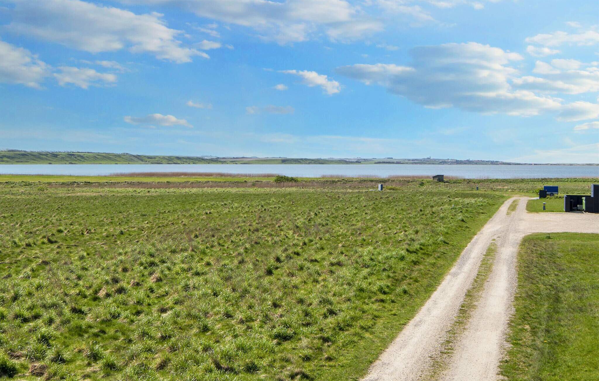 Un paysage rural avec un chemin de terre menant à un plan d’eau, le tout étant entouré de champs ouverts.