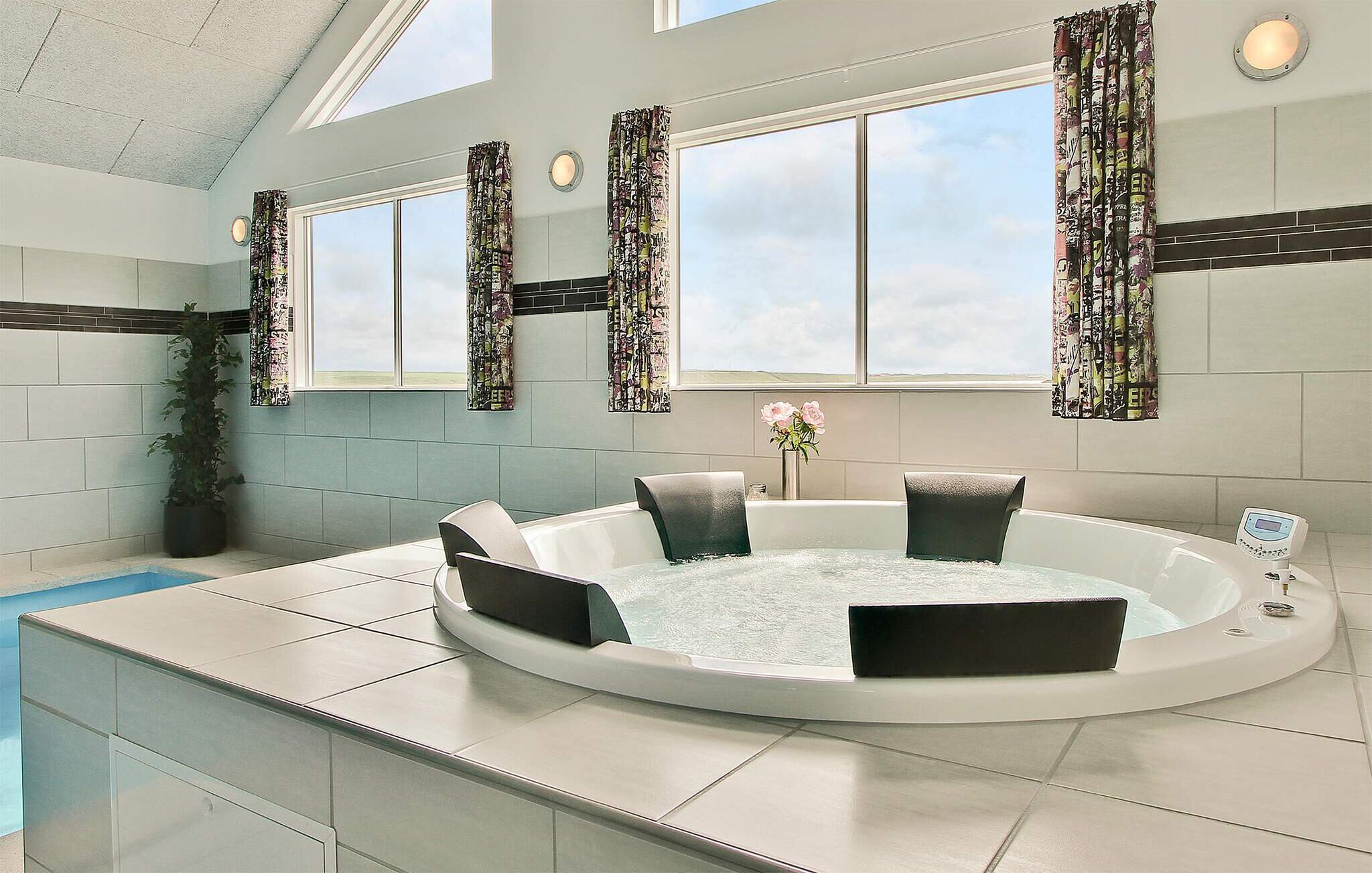A modern bathroom with a large bathtub, a potted plant, and a window with curtains.
