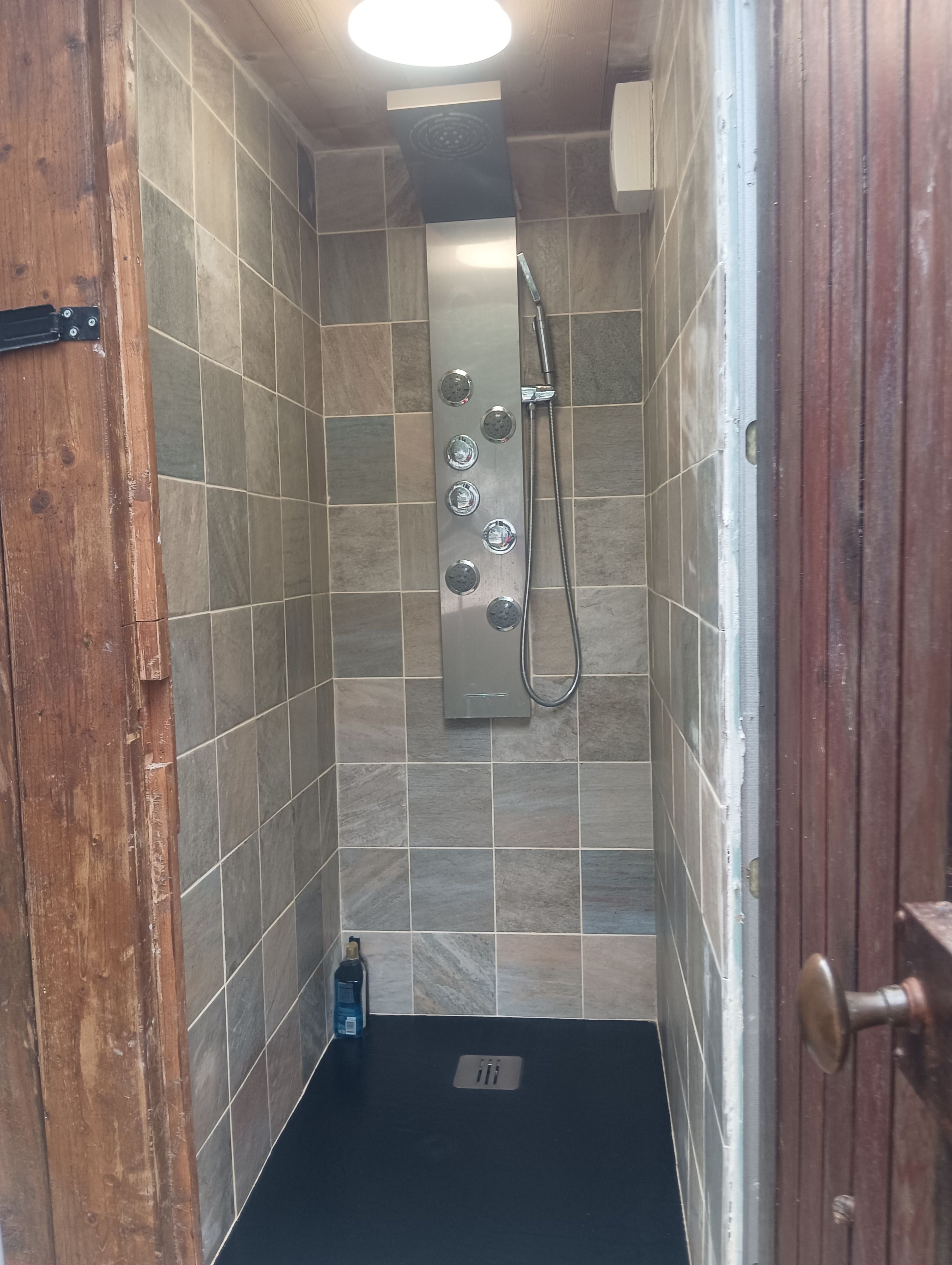 Un espace douche avec un mur carrelé, une douchette à main et un robinet à main.