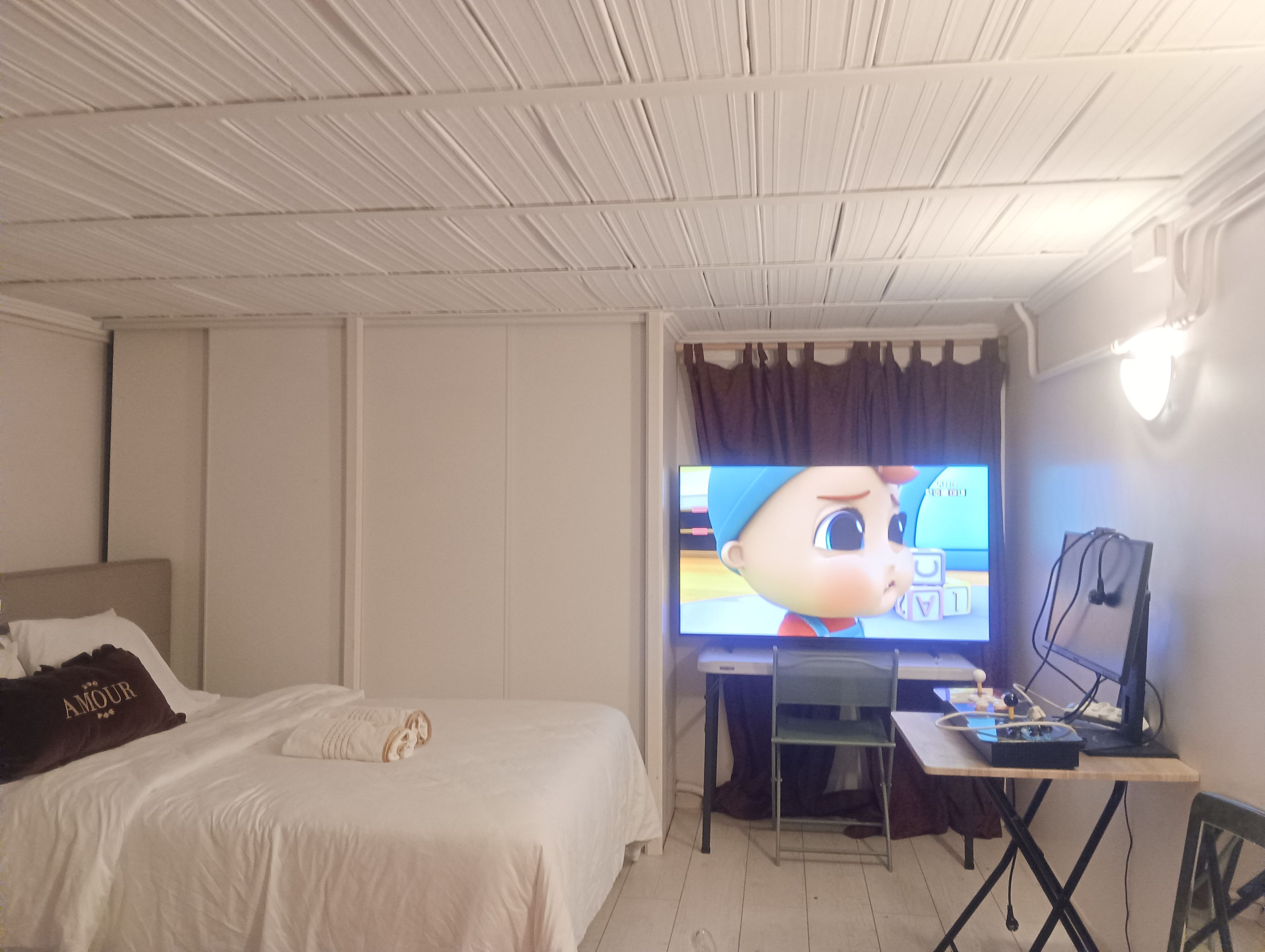 A hotel room with a bed, a desk with a computer, and a television displaying a cartoon character.