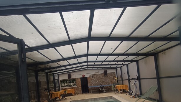 Ein Hallenbad mit gefliestem Boden, umgeben von Wänden, wobei eine Wand mit Steinverkleidung akzentuiert ist, und einer Metall-Dachkonstruktion.