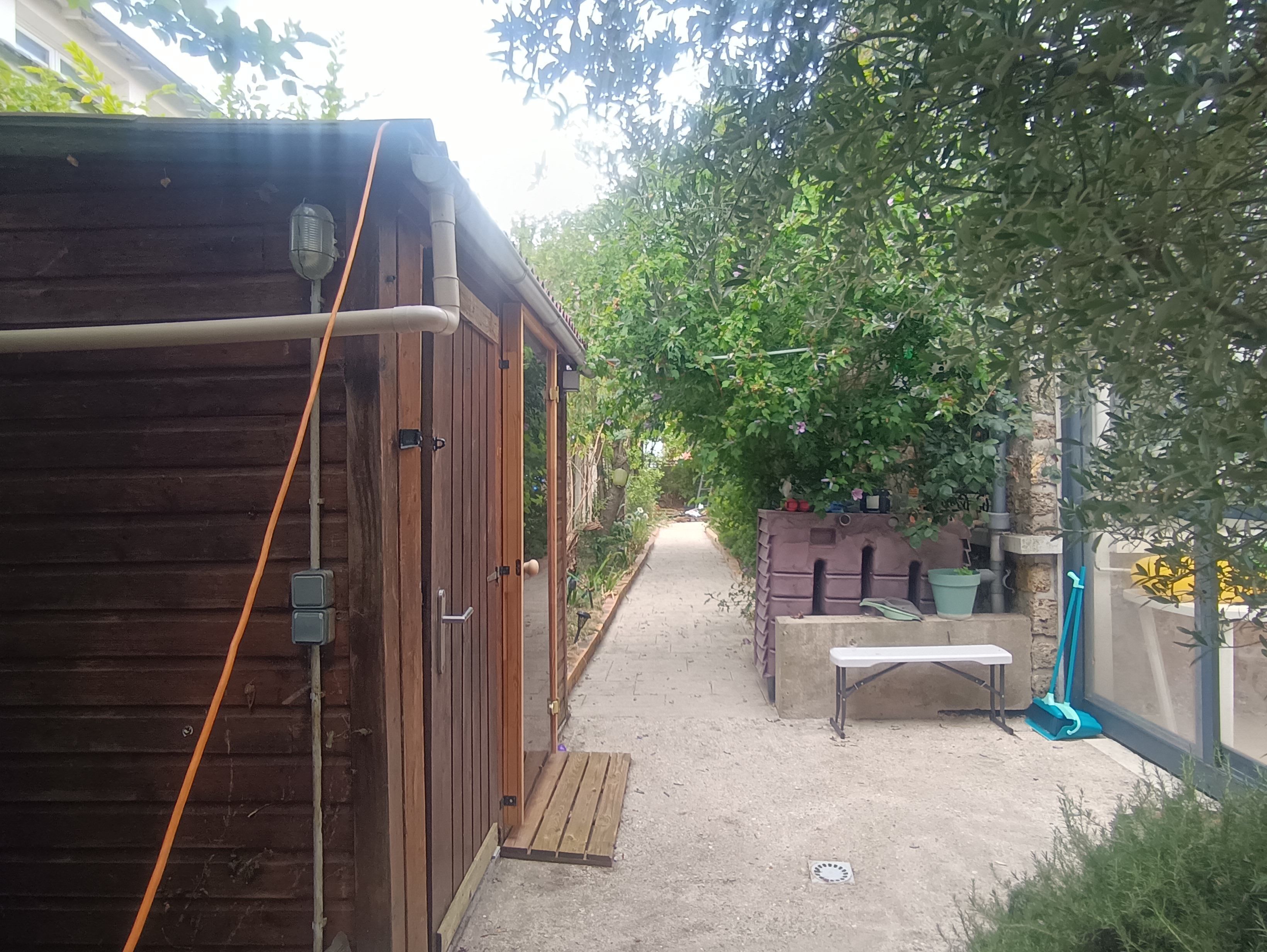 Une structure en bois dotée d’une porte, d’un banc et d’un chemin menant à un espace jardin.