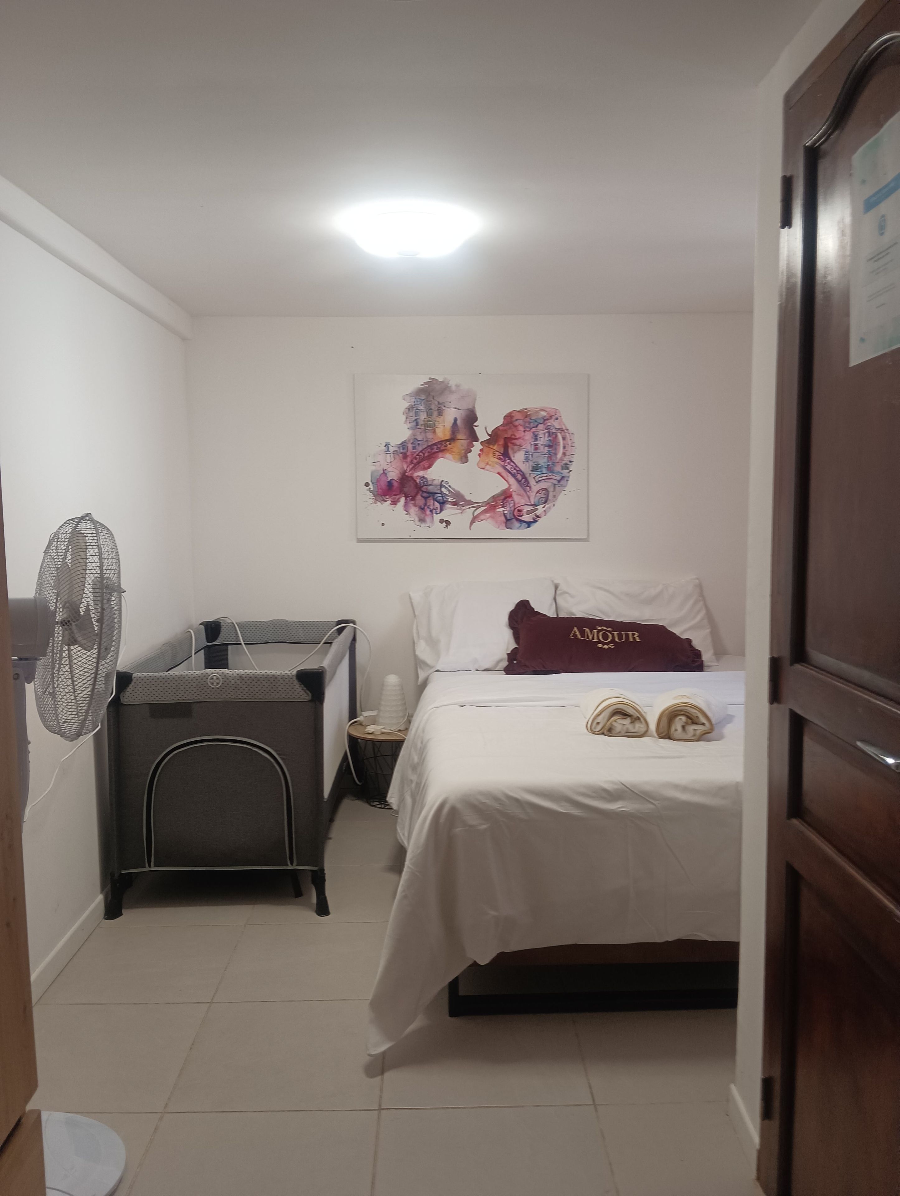 Une chambre d’hôtel comprenant un lit, une table de chevet, un ventilateur et une œuvre d’art accrochée au mur.