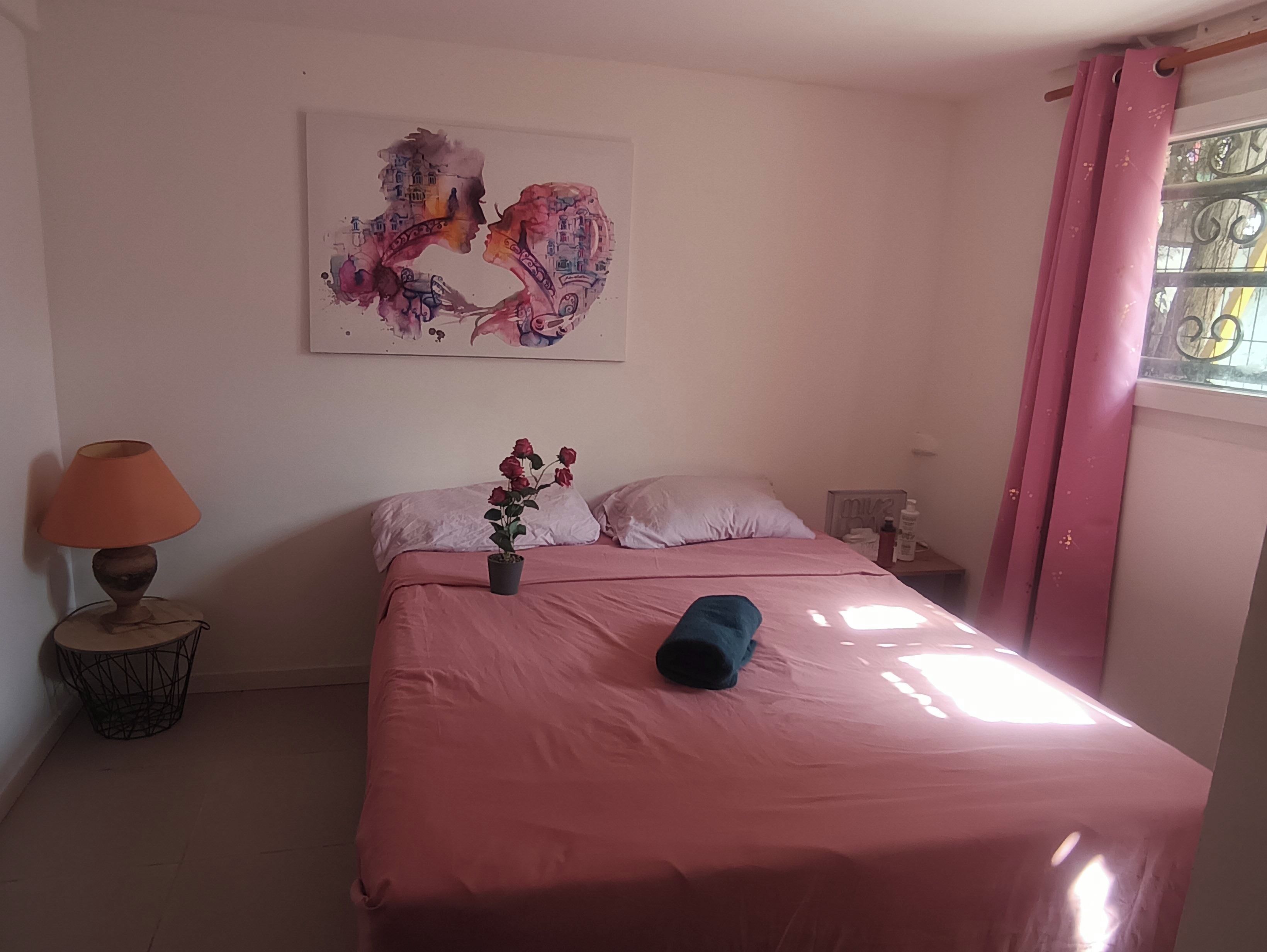 Une chambre à coucher avec un lit, une table de chevet, une lampe, une plante en pot et un tableau au mur.
