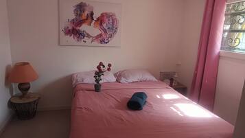 Une chambre à coucher avec un lit, une table de chevet, une lampe, une plante en pot et un tableau au mur.