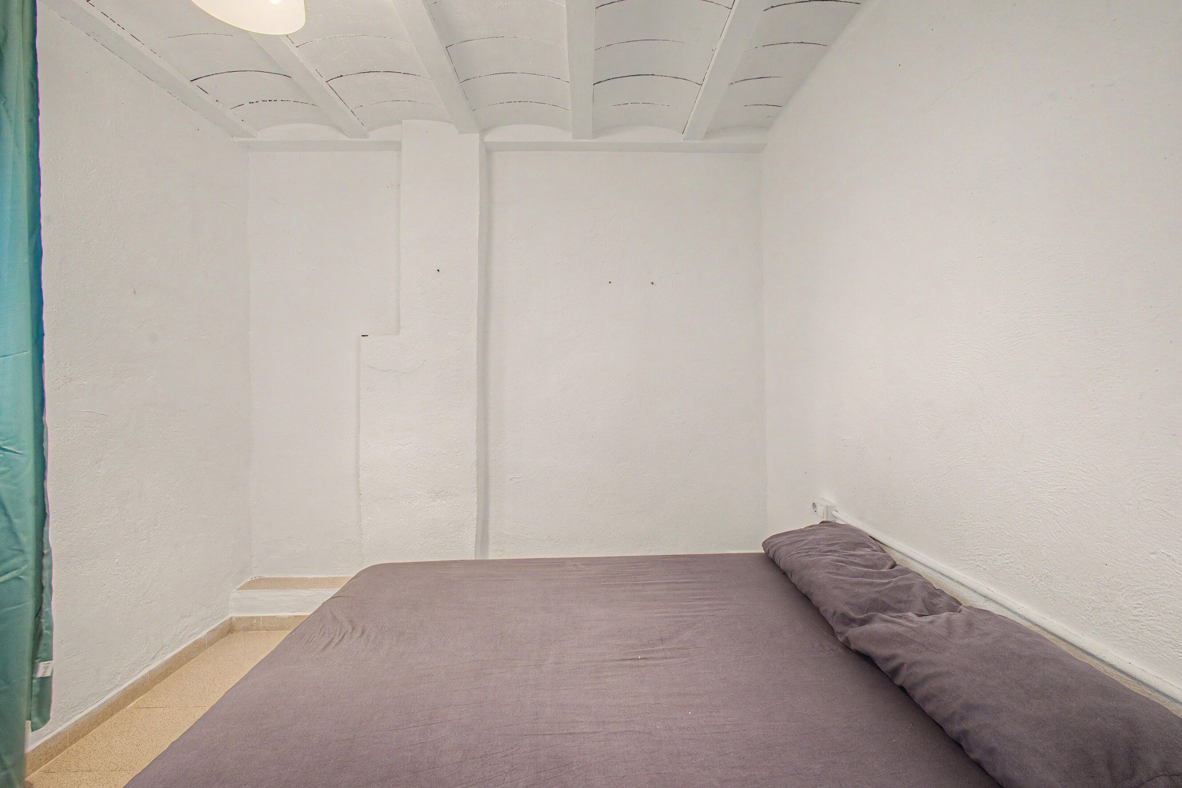 Ein Zimmer mit einem Einzelbett, weißen Wänden und einer schlicht gestalteten Decke.