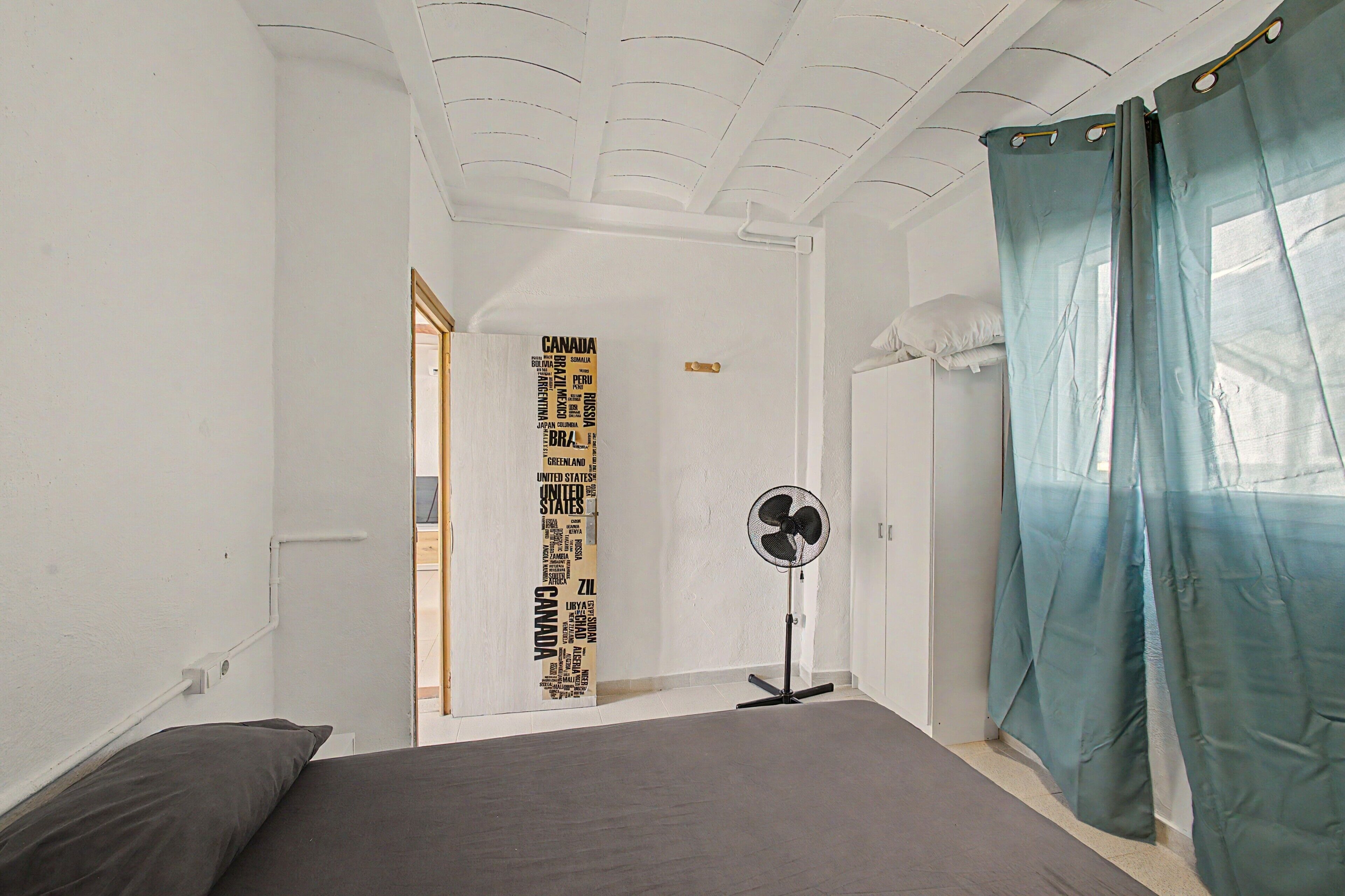 A bedroom with a bed, a standing fan, and a door with a world map.