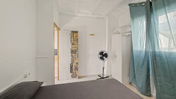 A bedroom with a bed, a standing fan, and a door with a world map.