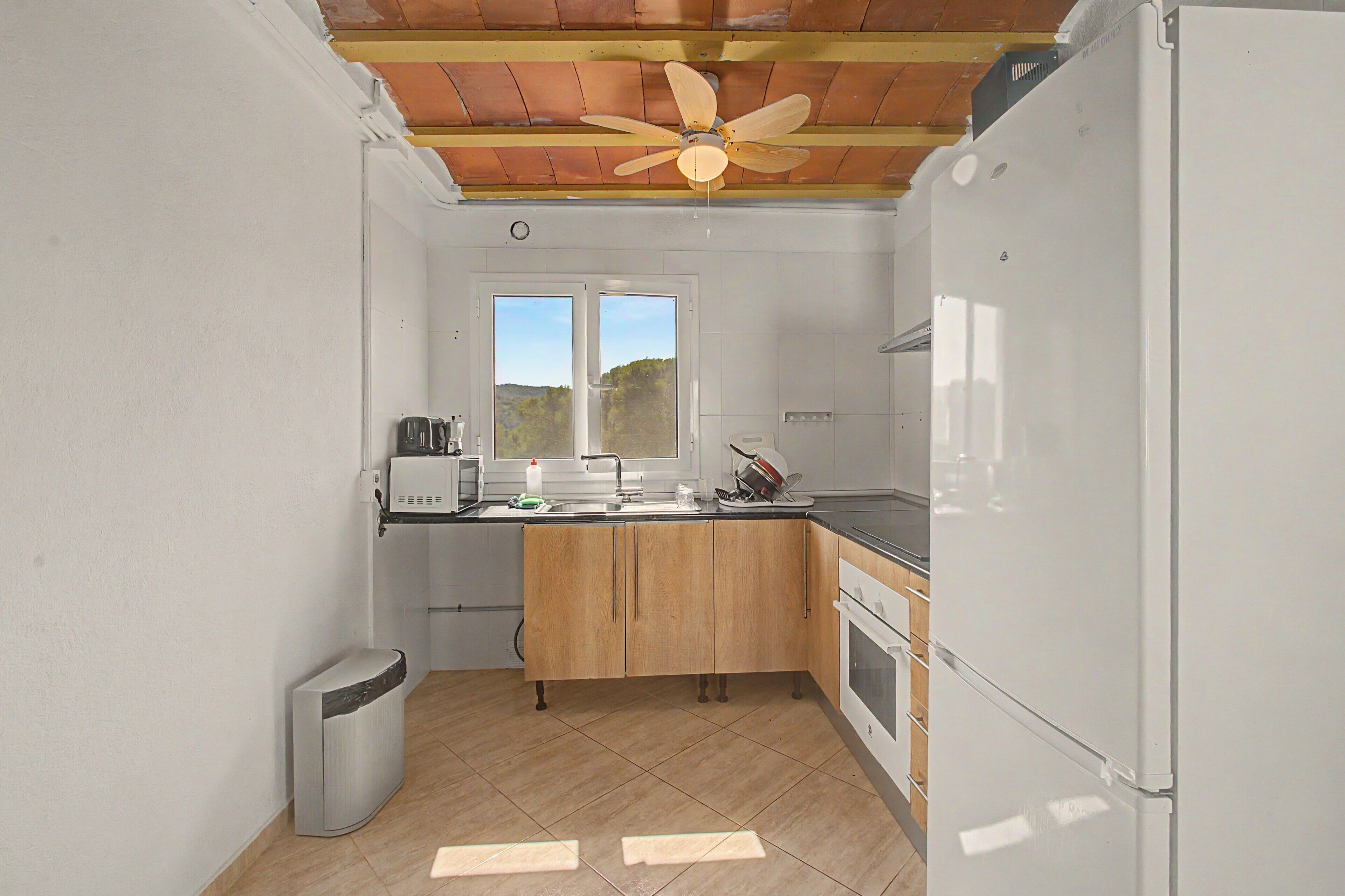 A compact kitchen with a built-in oven, a sink, and a window overlooking a natural landscape.