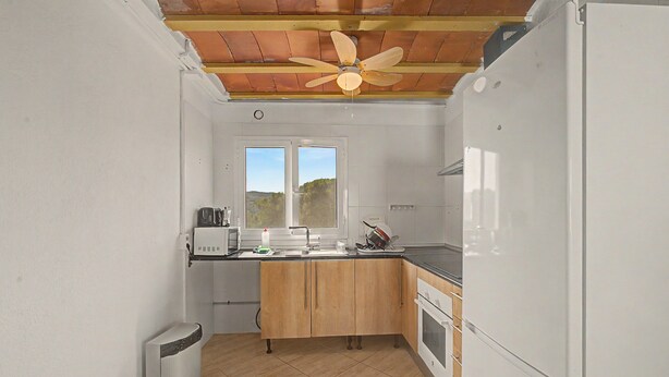 Cocina compacta con horno integrado, lavamanos y ventana con vistas a un paisaje natural.