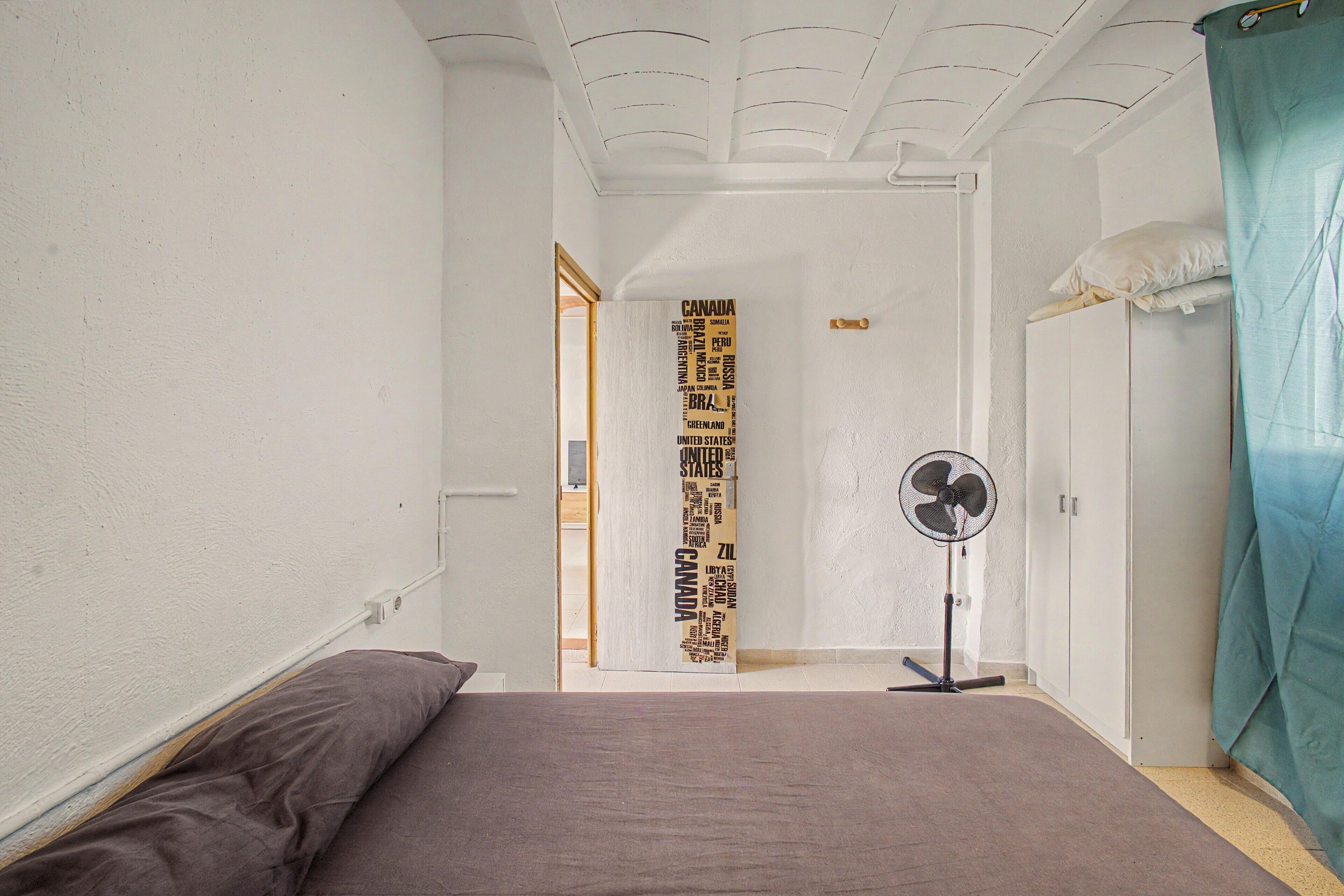 Un dormitorio con cama, ventilador y puerta que da a otra habitación.